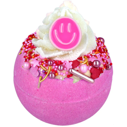 Pink bath bomb with white foam, pink smiley face, and decorative elements on a white background